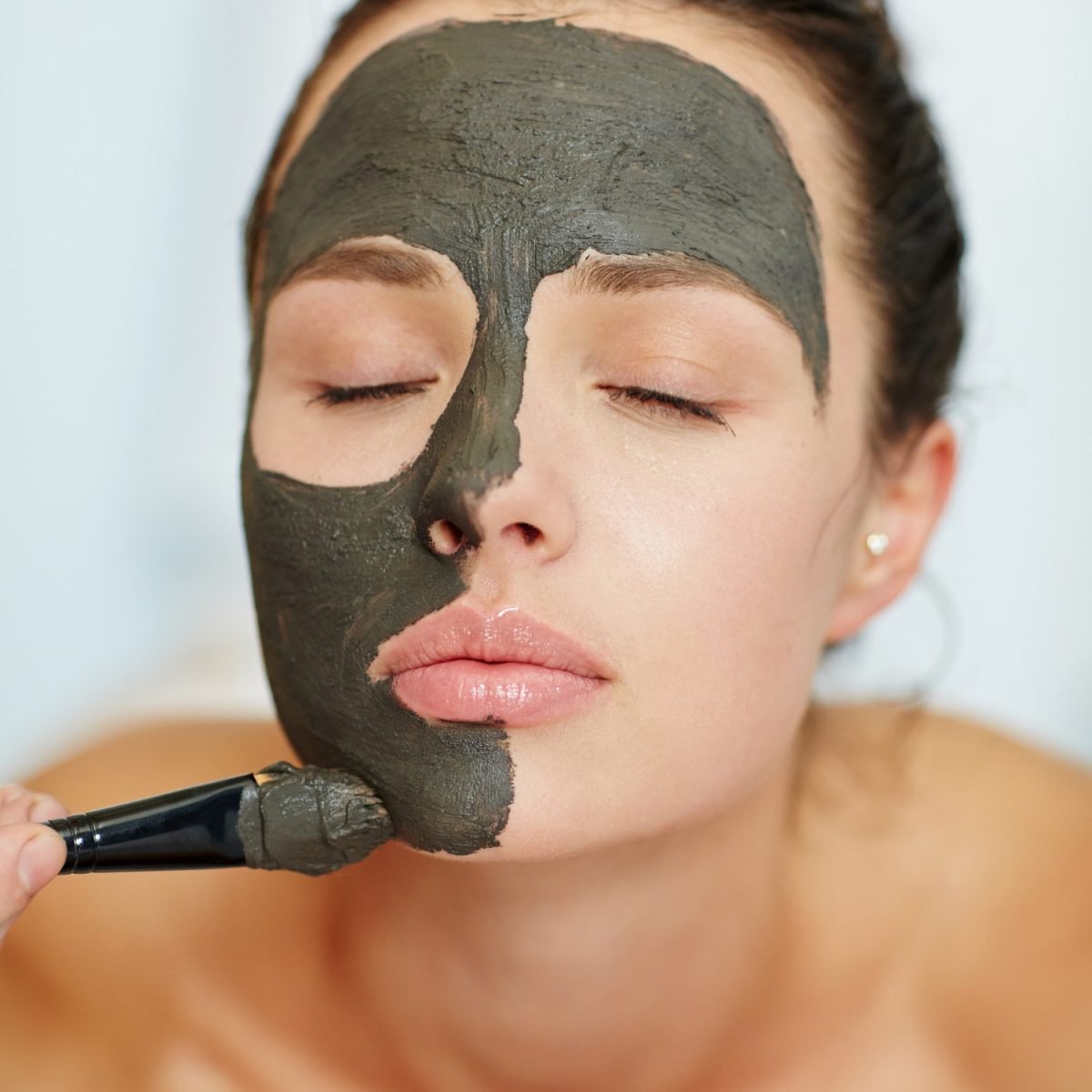 Young woman having rejuvenating clay mask on her face while visiting spa salon